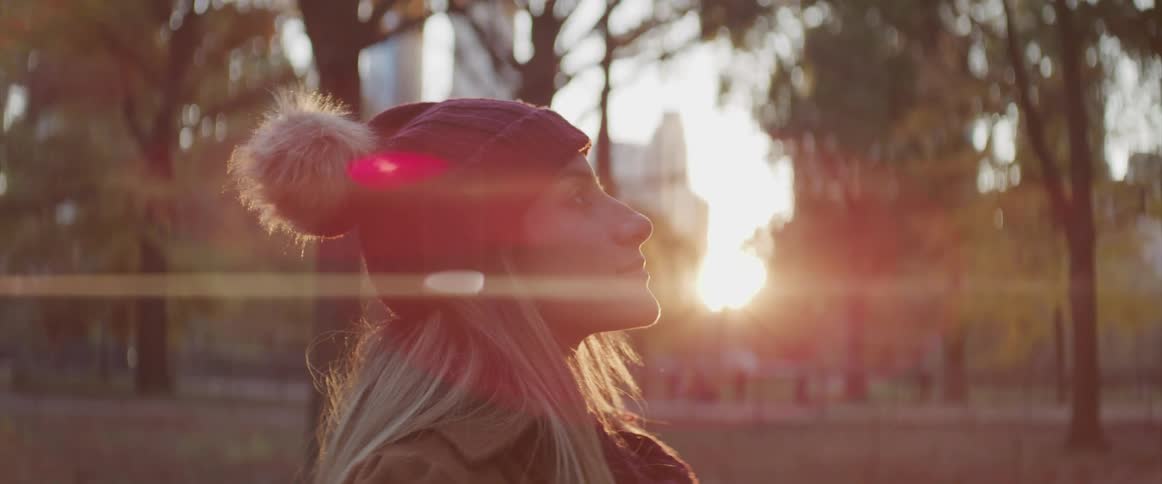 Blonde woman wearing a beanie closes her eyes and breaths deeply in the public park