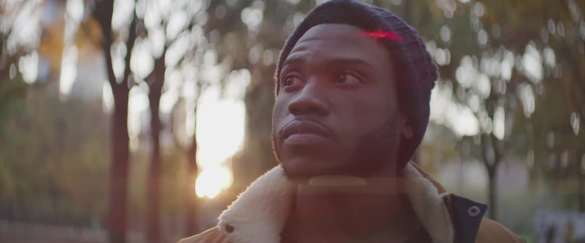 Black male looks to his right as he stands near the trees