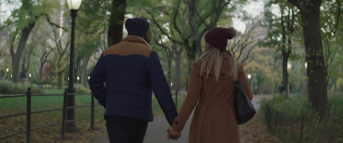 A man and woman holding hands while walking down a pathway in a park