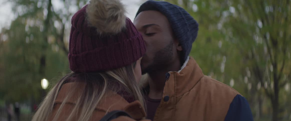 A man is kissing a woman in a forest area