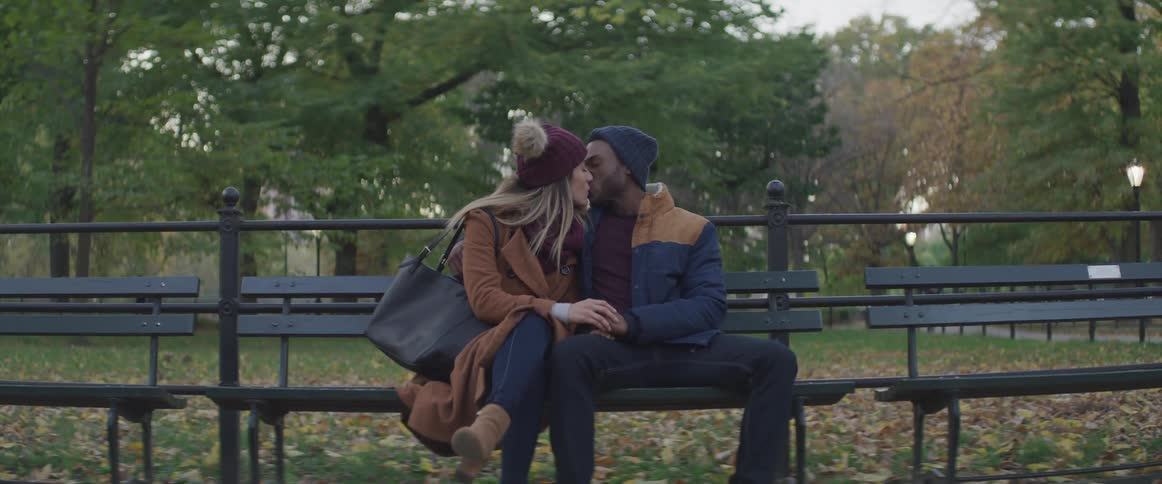 Couple sitting in bench on park hold hands while kissing