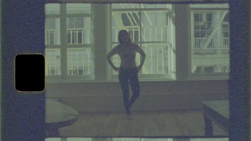 A woman does a simple dance in a living room in front of large windows