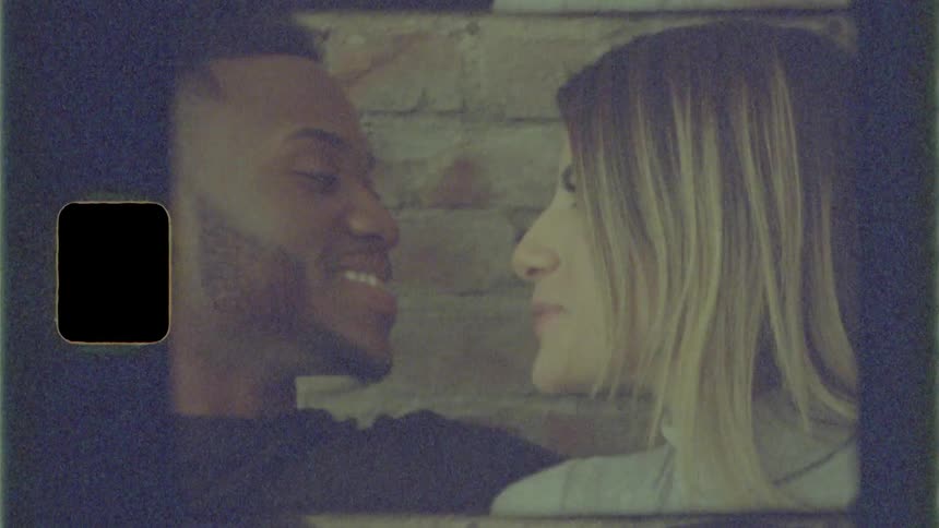 Black man and brunette woman sitting on the sofa kiss and talk to each other