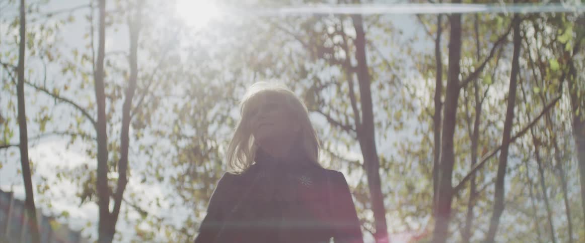 Woman stands and looks around while the sun shines bright in the public park