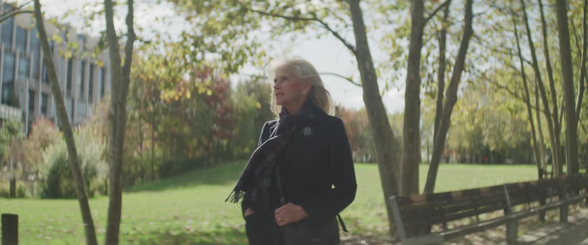 A woman stands outside of a building beside park benches on a pathway