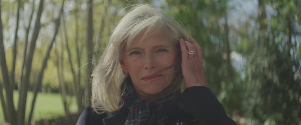 Woman turns her head and smooths her hair as she stands in a forest