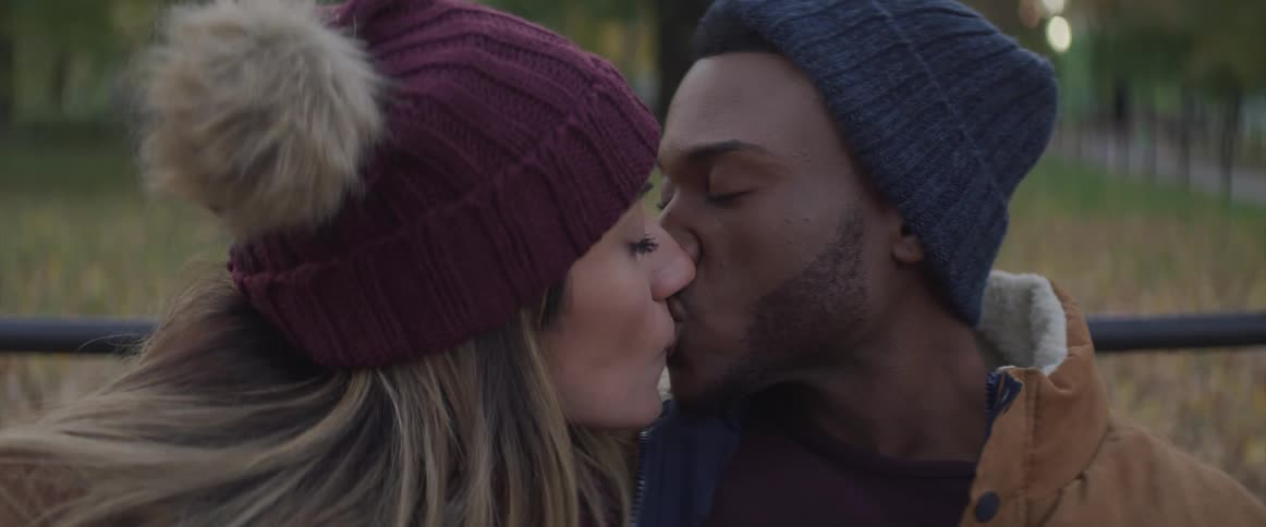 A woman kisses her boyfriend as they sit in a public park