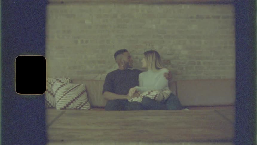 Male and female couple sitting close together on the couch holding hands while laughing talking and then kiss one another