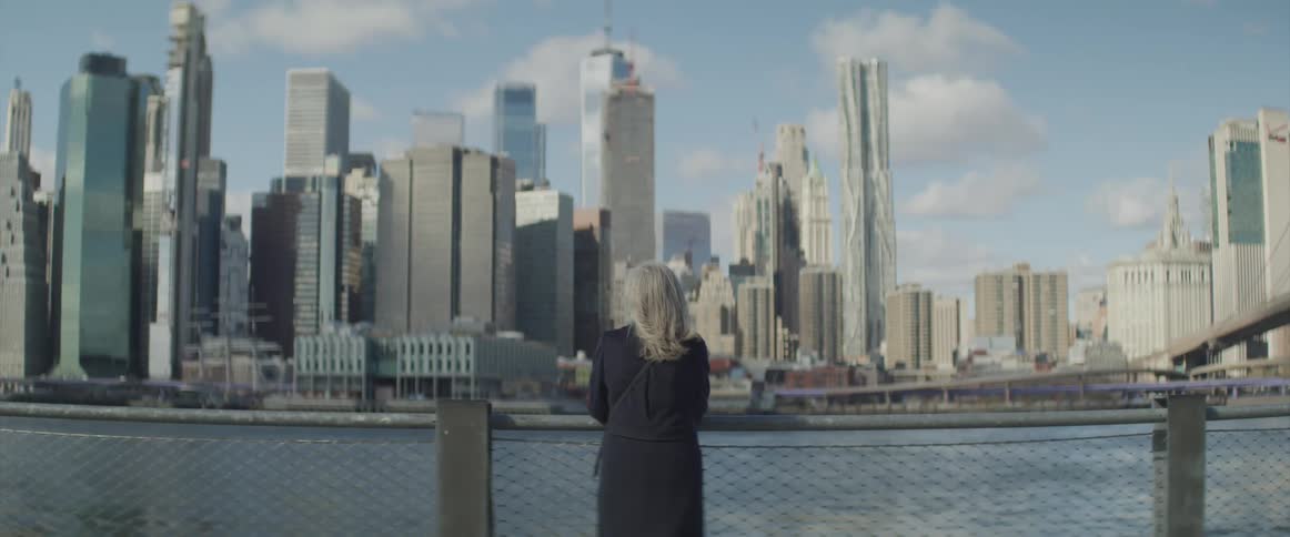 A woman stands in front of a lake and looks at the city skyline