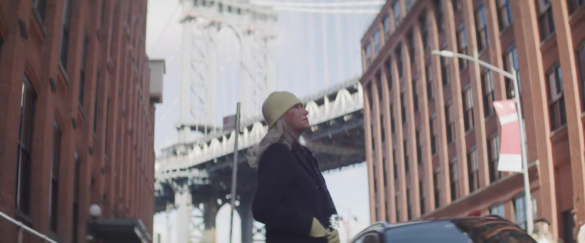 A woman stands in the street in front of the bridge