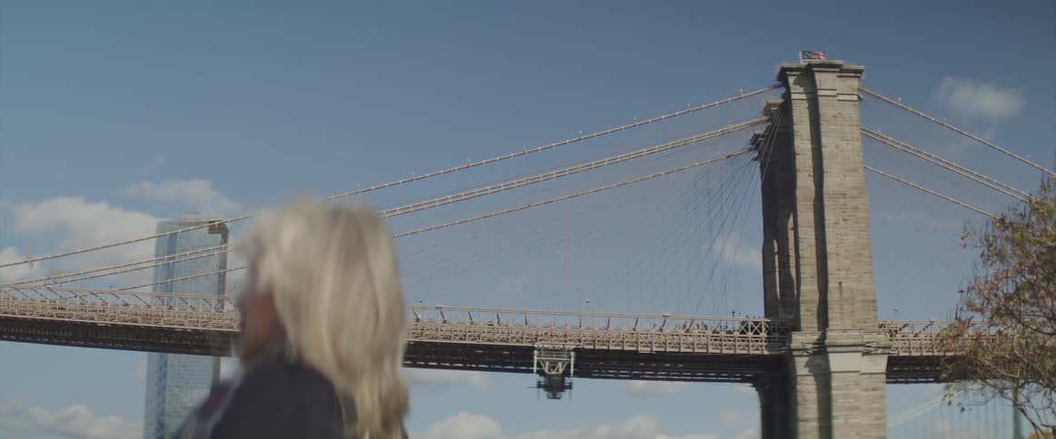 A woman stands in front of a suspension bridge