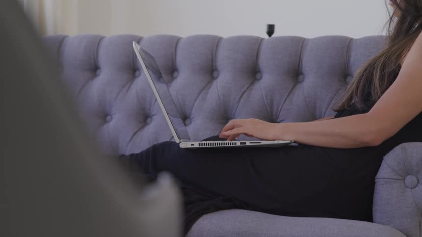 Woman sitting on the sofa types on her laptop in the living room at home