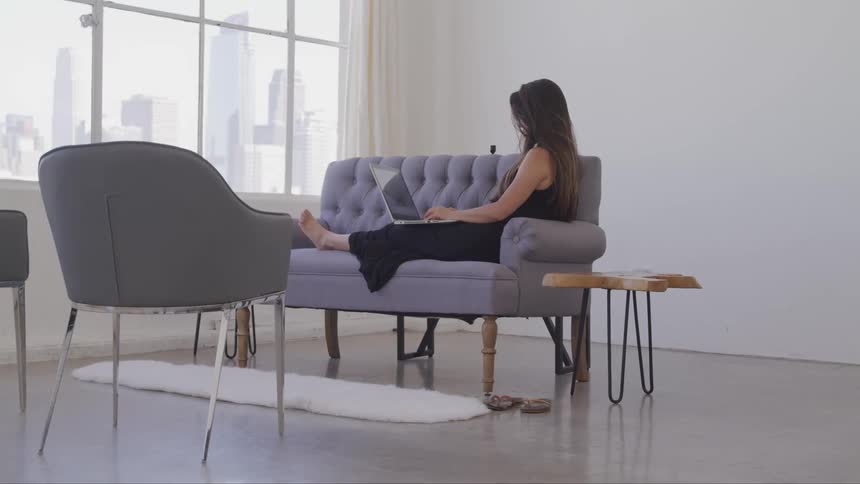 A woman is using her laptop on the couch