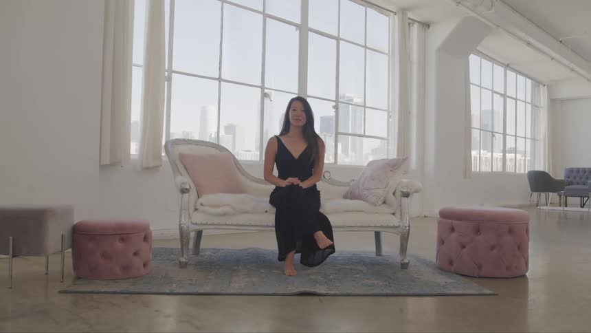 Asian woman wearing a black dress sit on the sofa and stares at the camera