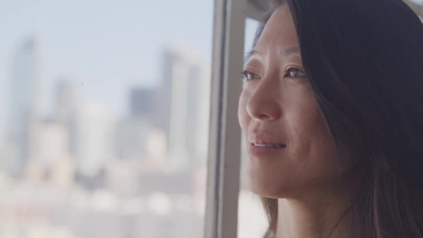 An asian woman gazing out of the window at the city outside