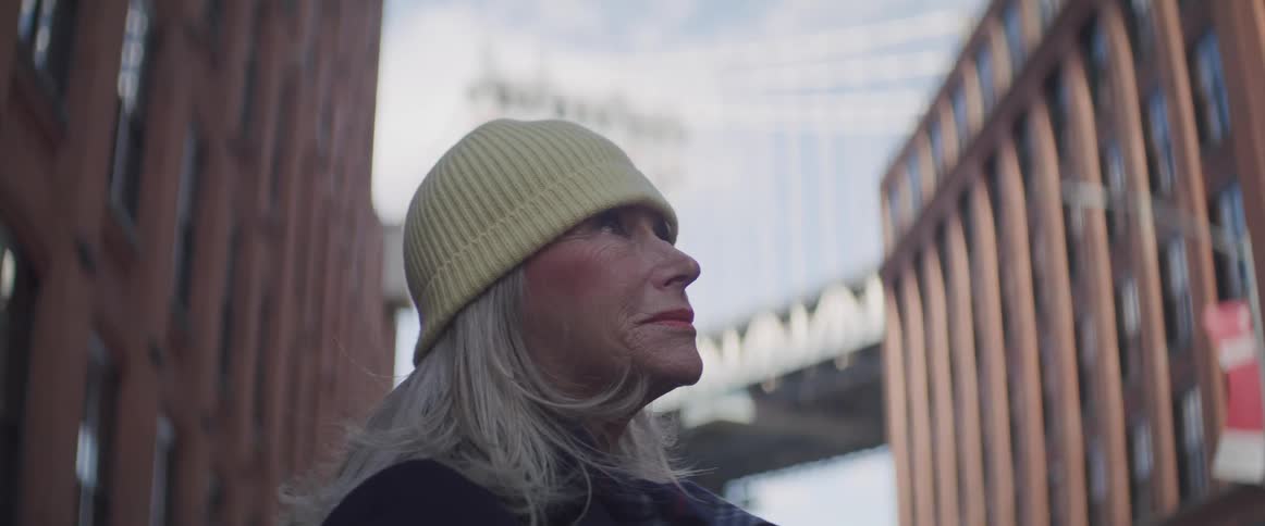 An elderly woman standing outdoors in a city looking upwards at something out of shot