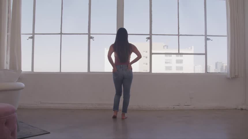 A woman stands in front of a large window looking out to the city