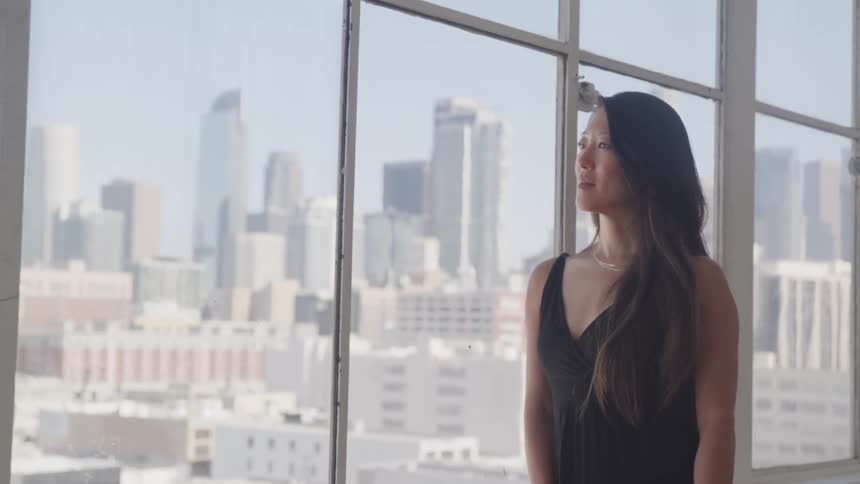 Woman with long hair stands near the windows as she looks out at the city