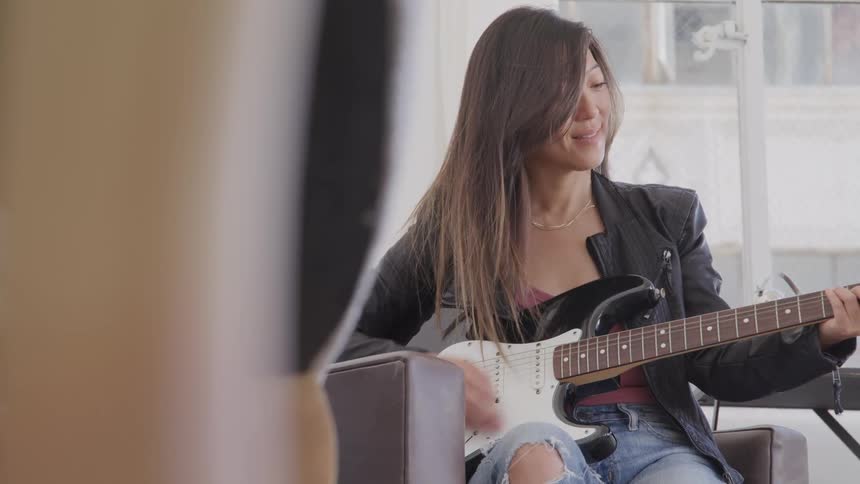 Woman with long dark hair playing an electric guitar indoors