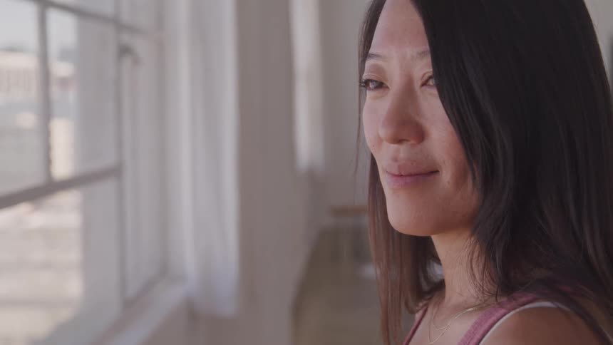 Asian woman standing by a window indoors and looking out