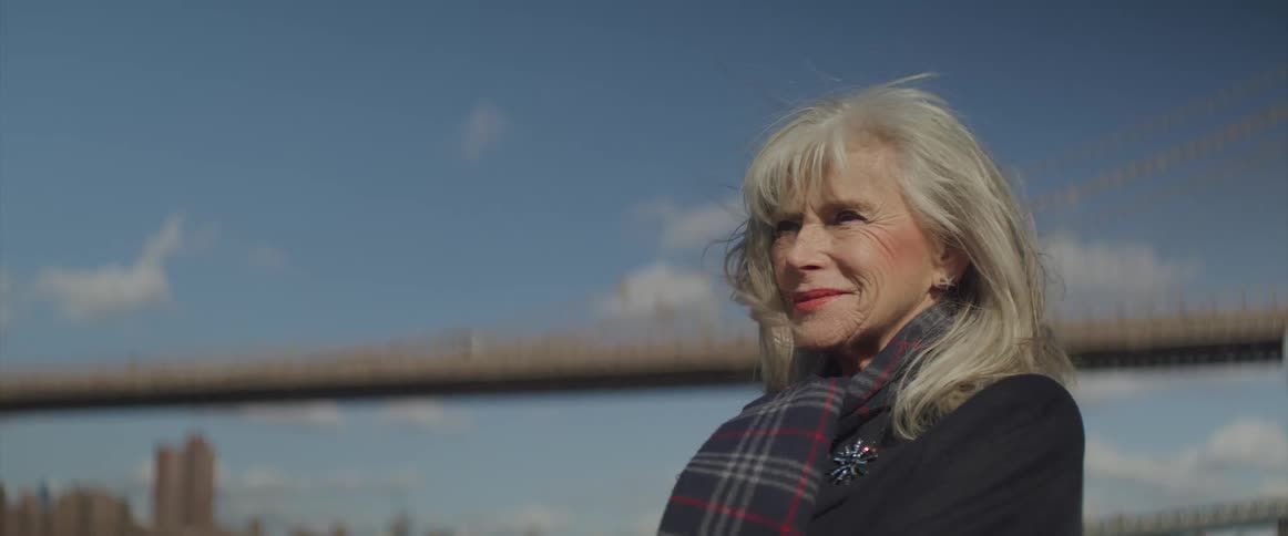 Elderly woman stands near bridge while the wind blows her hair