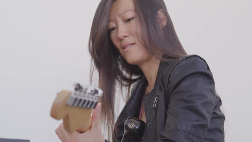 A woman sits and plays electric guitar