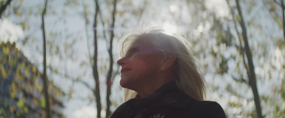 An elderly woman stands outside and looks around and smiles
