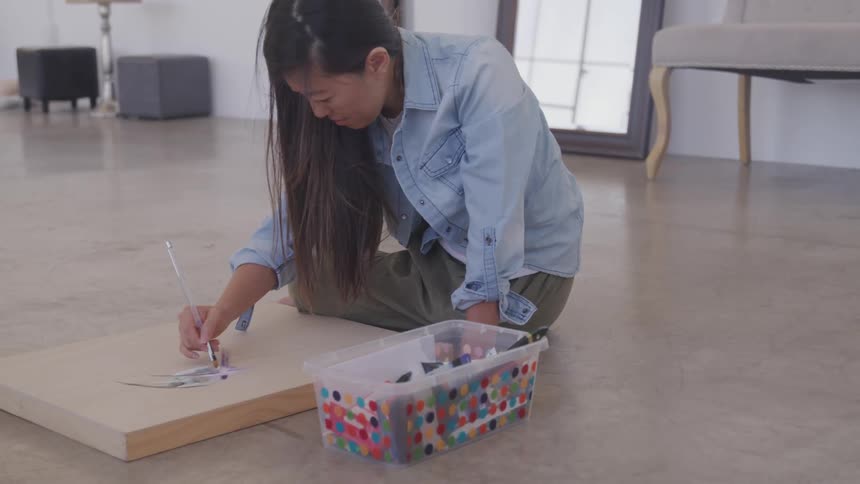 Woman sits on the floor and painting with paintbrush on wooden board