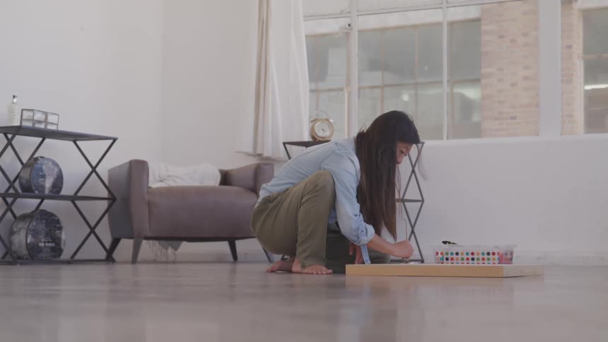 A woman kneels on the floor painting