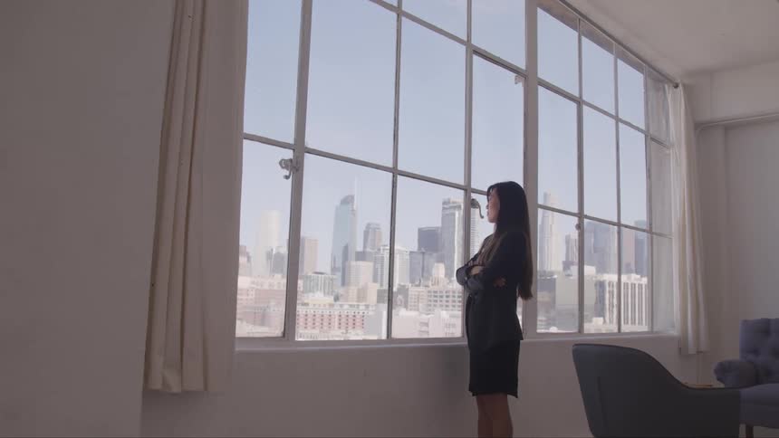 A woman in a business suit stands next to a large window in an office downtown