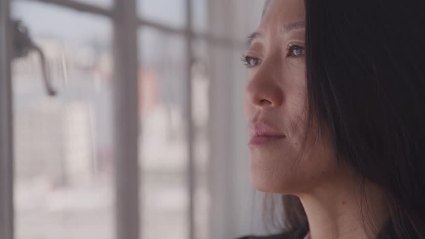 Asian woman looking out the window of apartment in the city