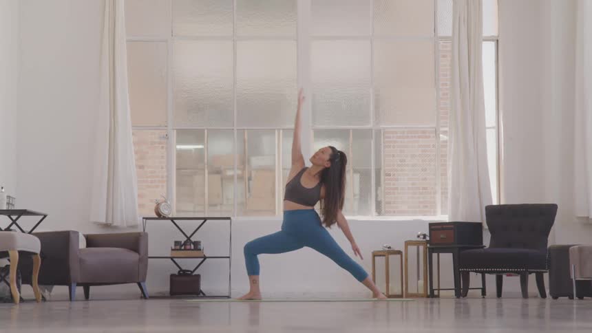 Woman with long dark hair doing yoga in front of large window indoors