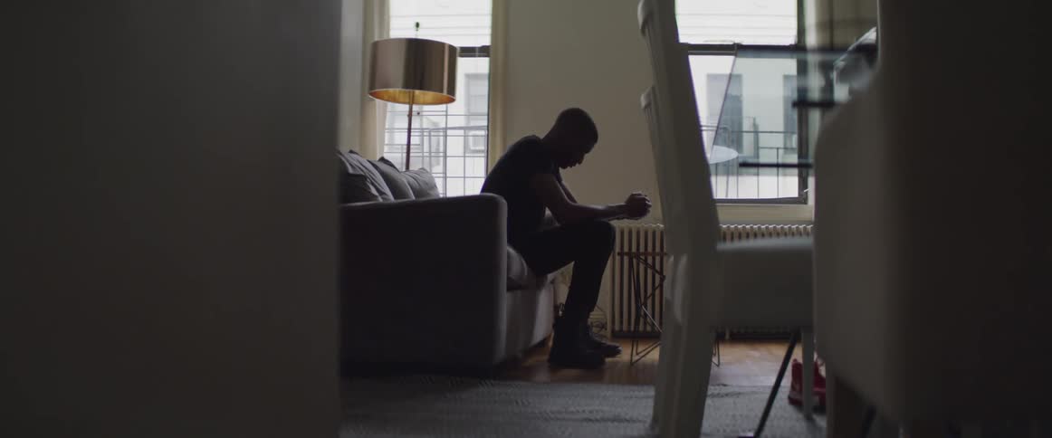 Depressed looking male sitting on couch in living room with his arms resting on his lap and his holding his handing together