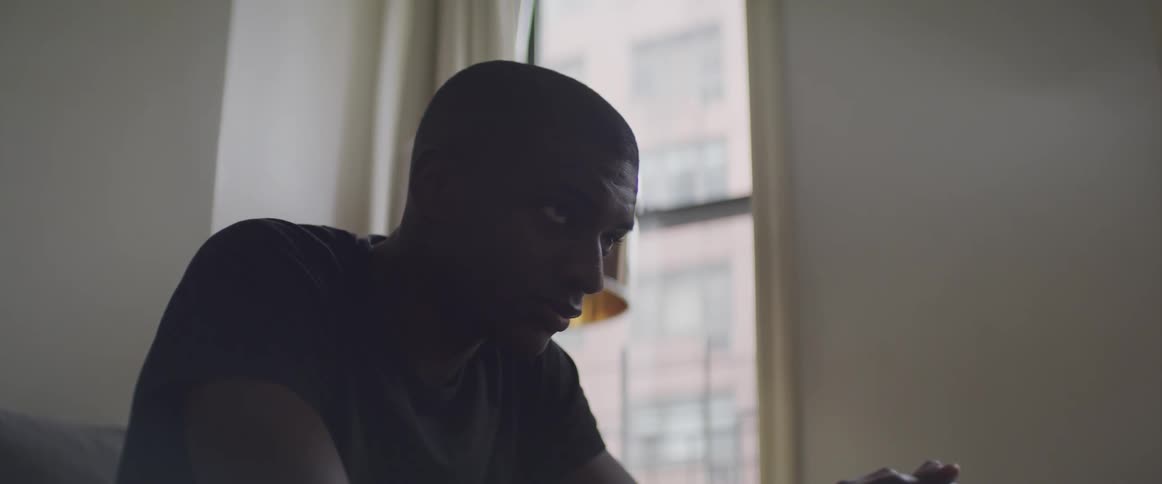 Black man sitting on the sofa raises his head and looks ahead in a room