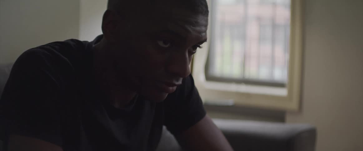 Black man sitting on the sofa raises his head and looks ahead in the living room