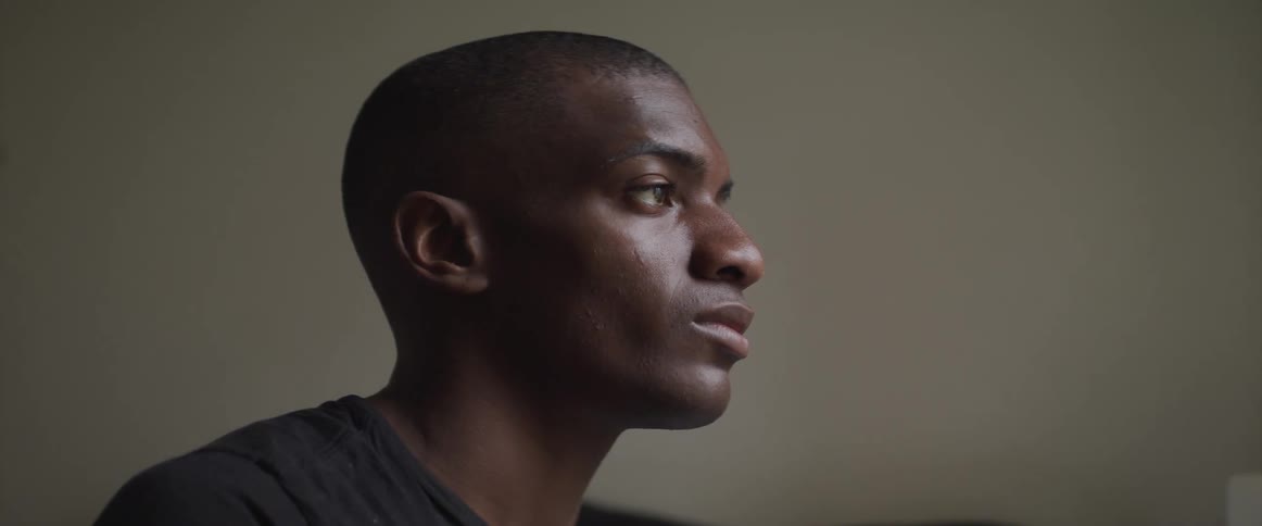 Side view of a black man looking ahead on a gray background