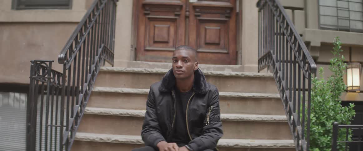 Black man sitting on steps of front porch of an apartment