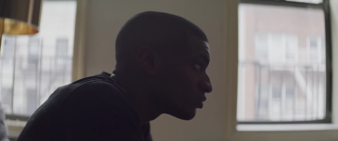 Black man sitting on the sofa raises his head and looks ahead in the room