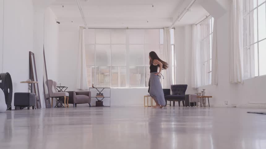 A woman dances in a large space with little furniture