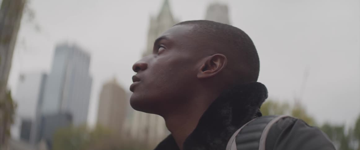 Side view of a black man looking up at the high rise buildings in the city