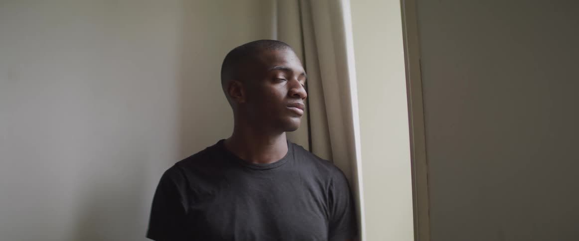 Black man looking out the window turns his head and stares at the camera