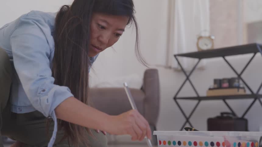 A woman kneels to the floor painting with a paintbrush