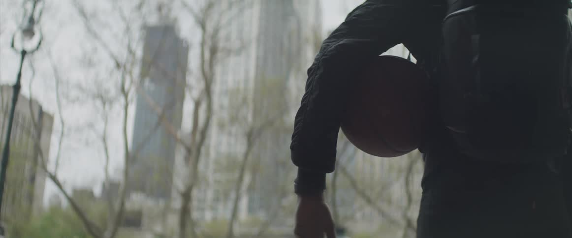 A person with a backpack holding a basketball under their arm with buildings in the foreground