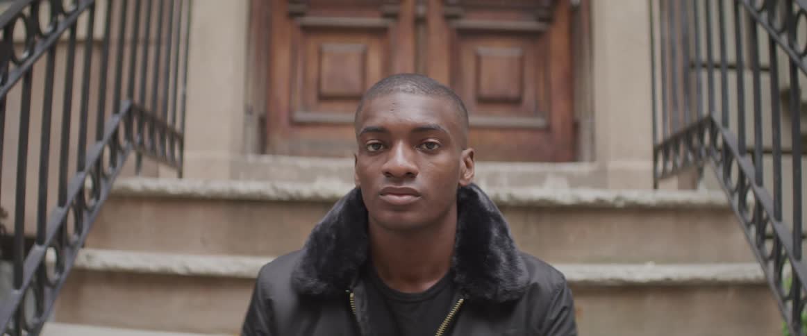 Black man sits on a step and turns his head to look at the camera