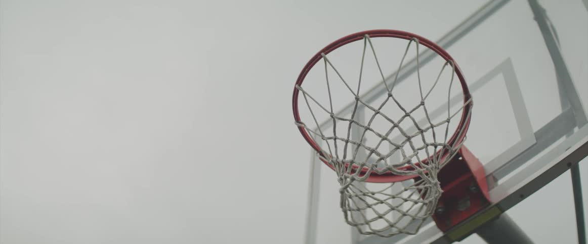 Cloudy sky shows through clear backboard of basketball hoop