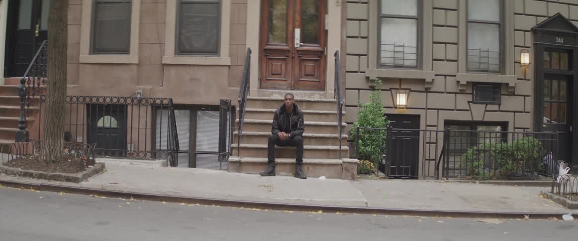 Black man sitting on front steps of apartment building in a neighborhood