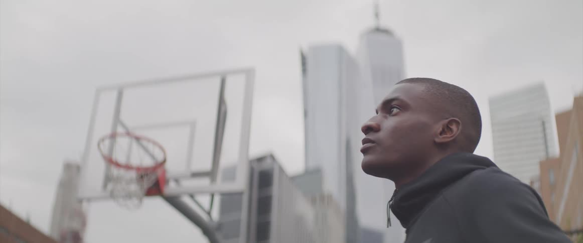 A man standing by a basketball hoop looks off in to the distance