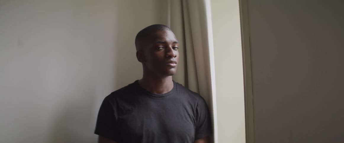 Black man looks out the window and turns his head to the camera