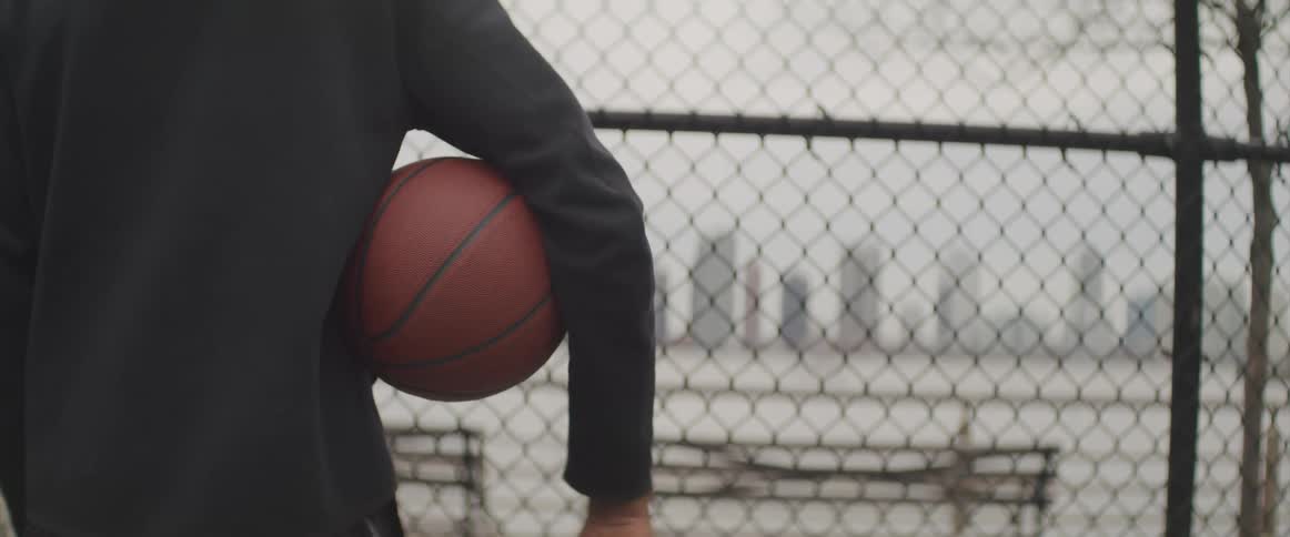 A person standing in front of a chain link fence with a basketball under their arm