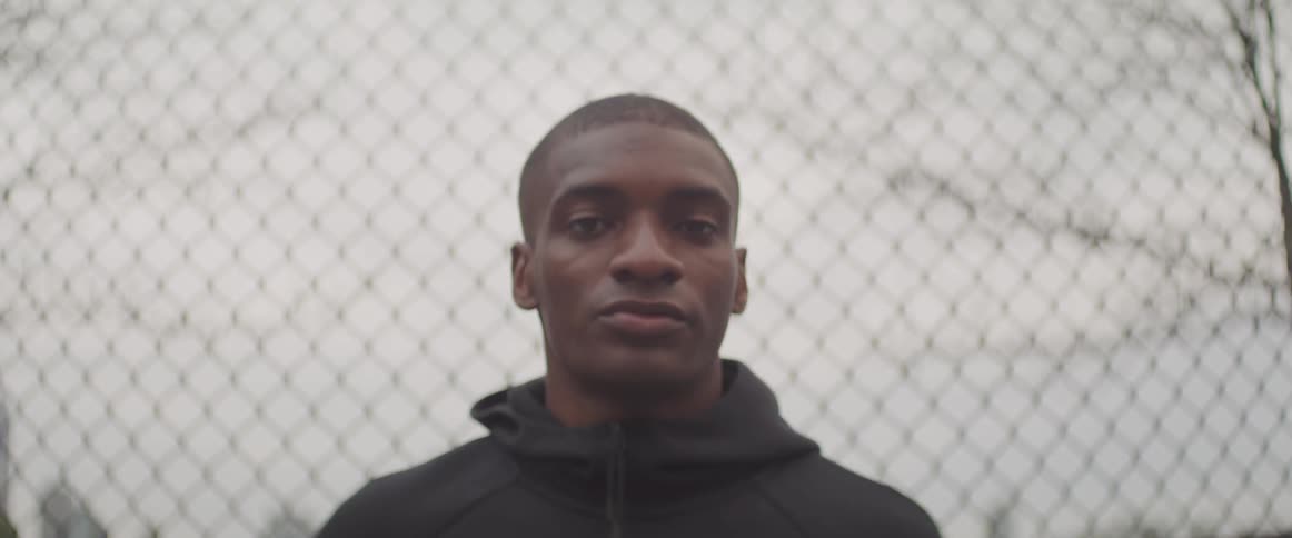 A man turns his head and starts to stare with a chain link fence in the background
